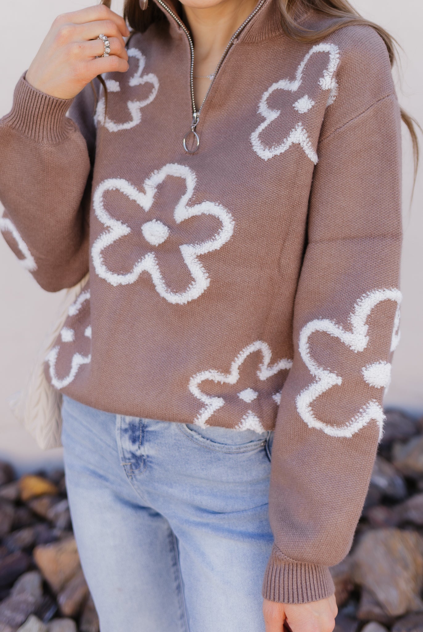Person wearing a brown sweater with white floral patterns outdoors.