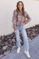 Woman wearing a floral blouse and jeans standing outdoors with rocks and a wall in the background