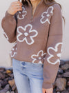 Person wearing a brown sweater with white floral patterns outdoors.