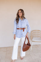 Woman wearing a blue striped shirt, white pants, and carrying a brown handbag indoors.